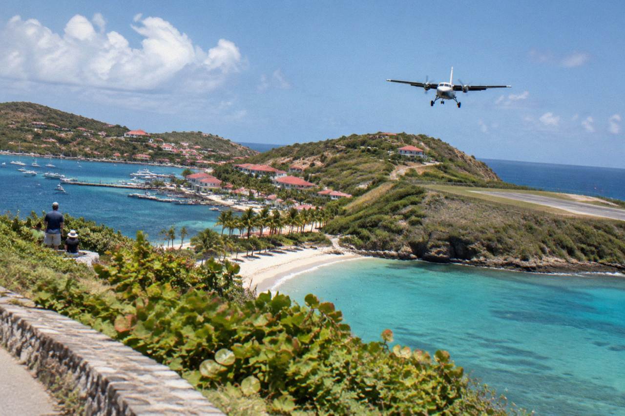 A small turboprop on final approach over a hill above a Caribbean beach town