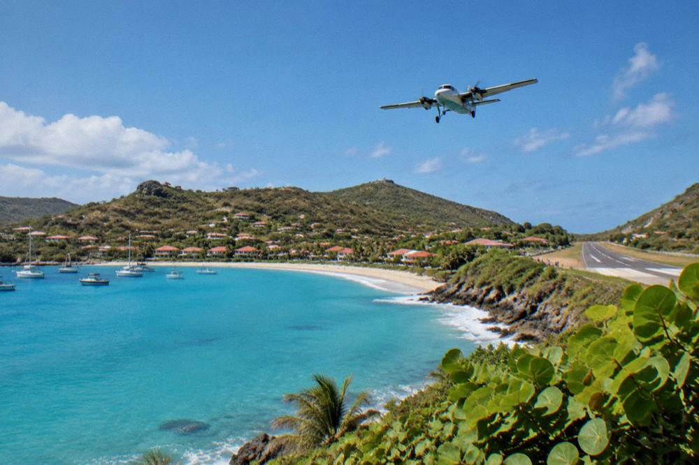A turquoise bay with a white-sand beach and a small airstrip at its far end
