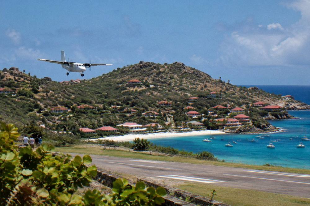 A small aircraft on the ground at a Caribbean airstrip with hills behind