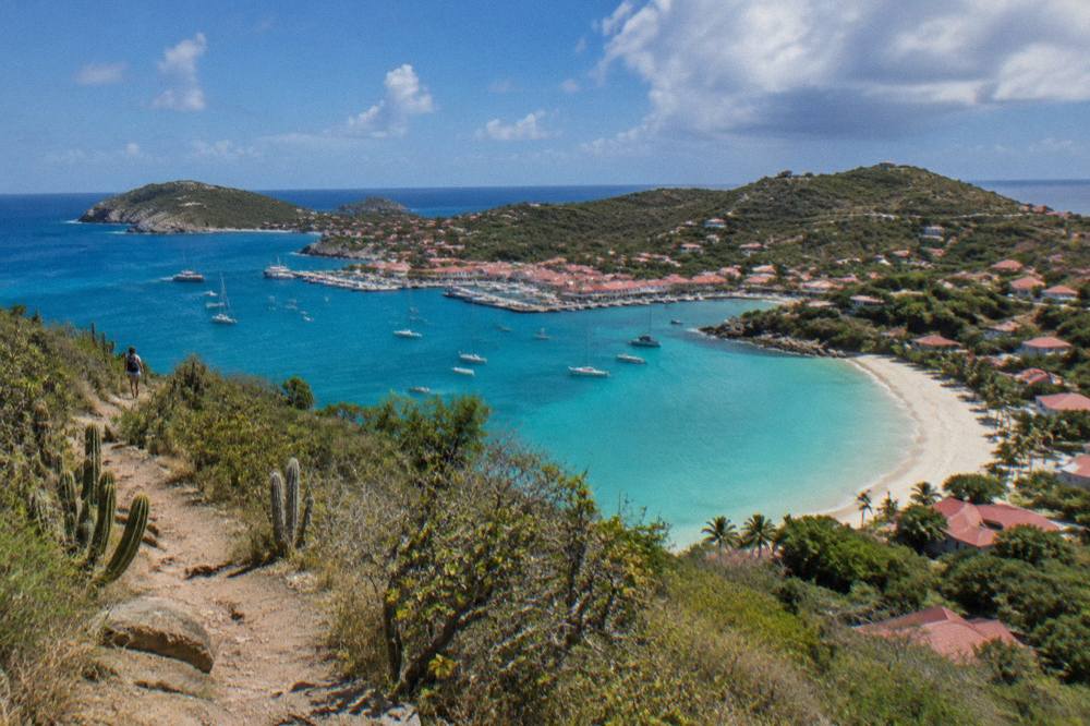 Turquoise water and a pale sand beach seen from a grassy headland path