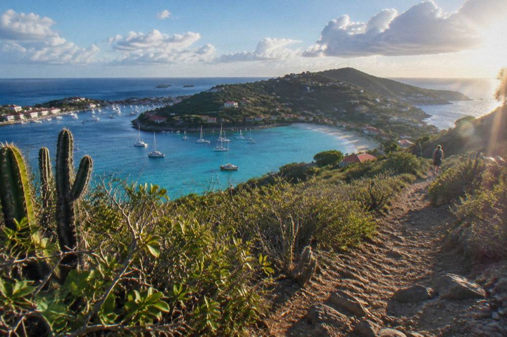 A pale sandy beach enclosed by green hills and clear shallow water