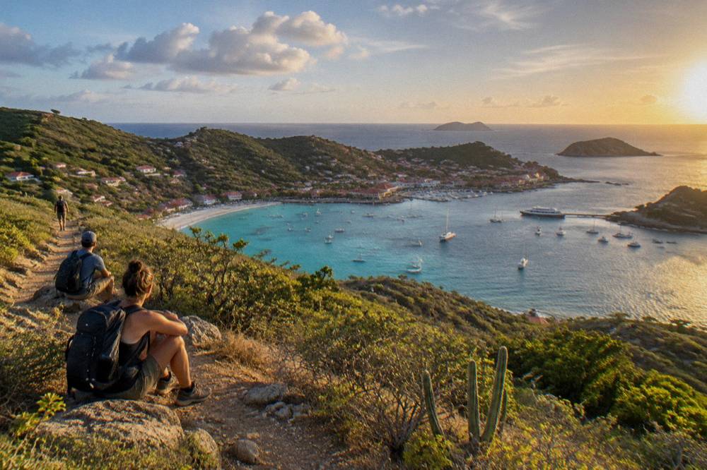 Hikers with backpacks resting on a sunlit coastal hillside overlooking the sea