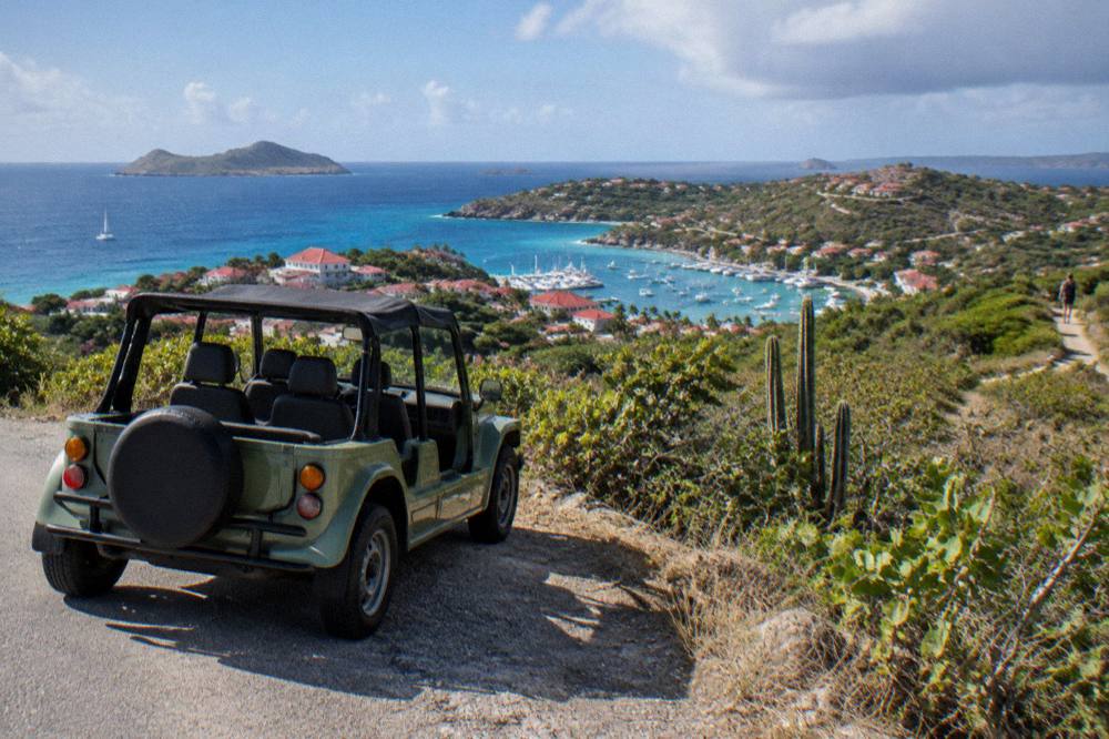 A small open-top rental car parked beside a narrow island road with sea views