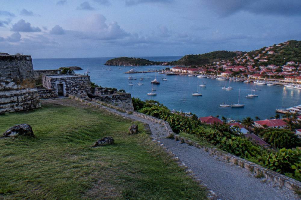 Old stone fortification walls on a green hill overlooking a harbor town