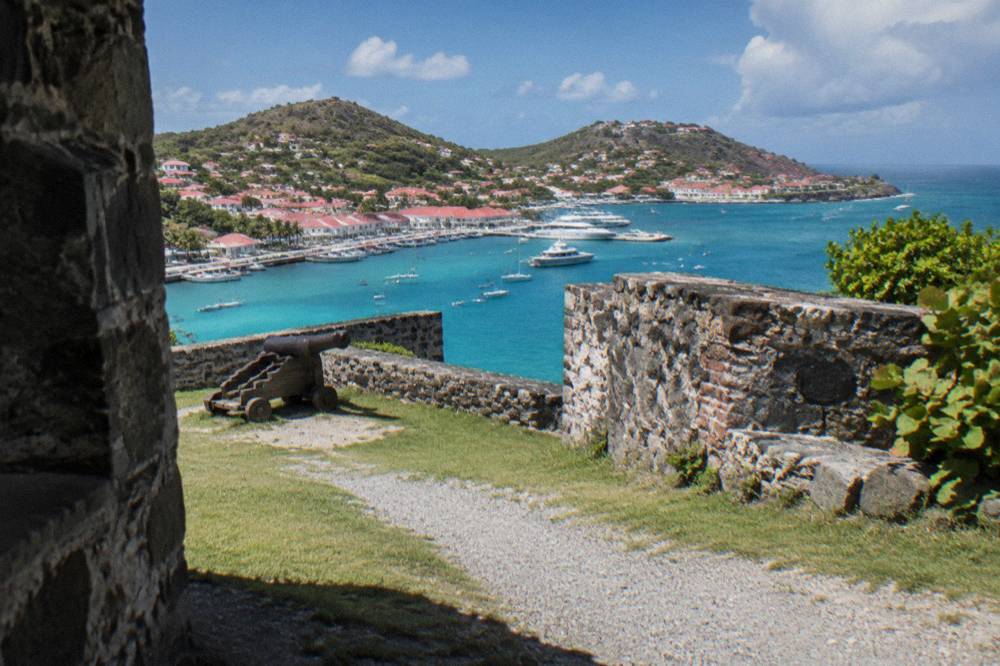 A small Caribbean harbor town seen from a hillside with red roofs and turquoise water