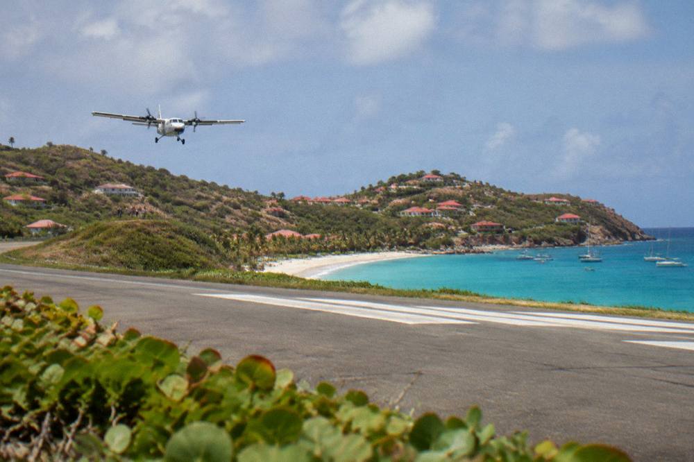 A small turboprop aircraft on a short runway beside a Caribbean beach