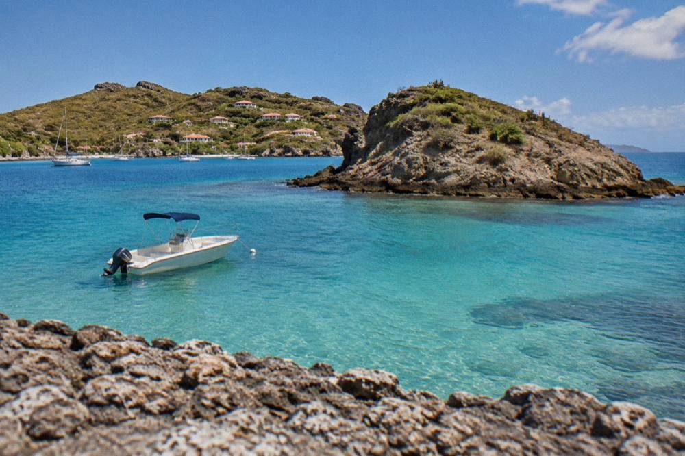 A small boat anchored in clear shallow water beside a rocky islet