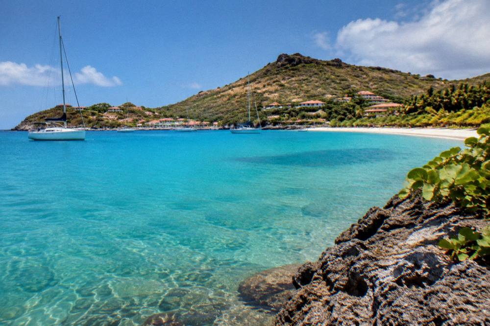 A calm bay with boats at anchor and wooded slopes behind the shore