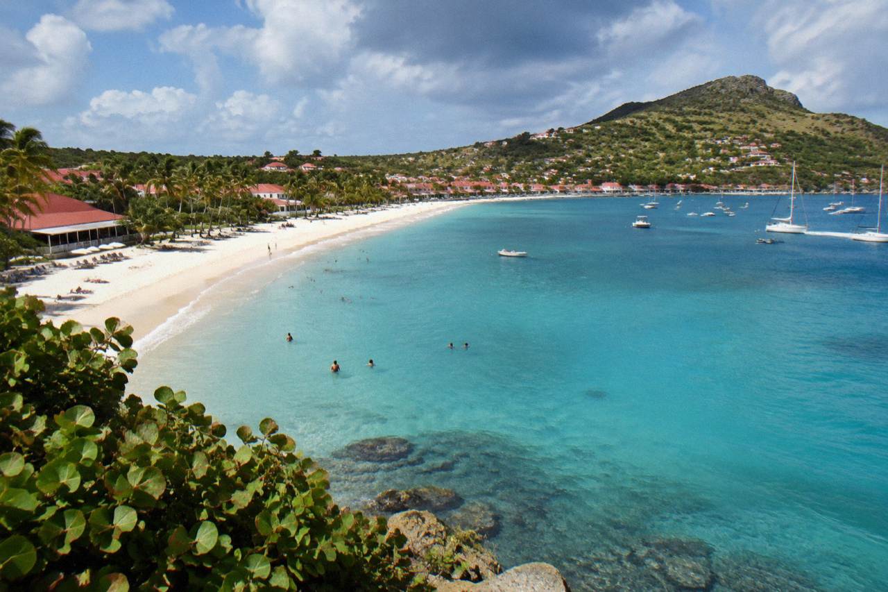 A curved bay of turquoise water with low hills and a seaside village along the shore