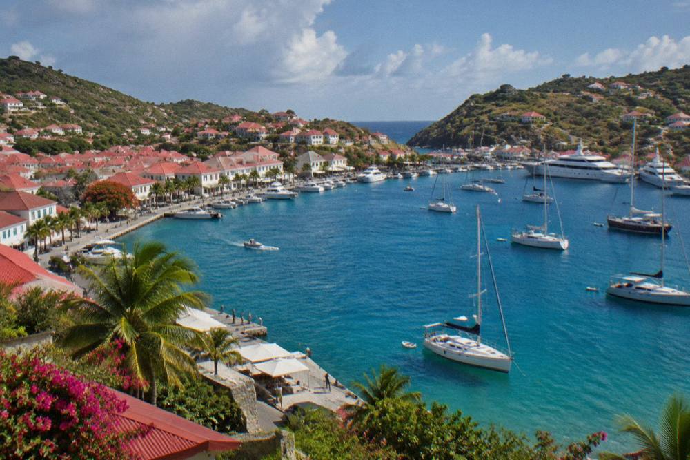 Yachts moored in the U-shaped harbor of Gustavia with red roofs climbing the hillside