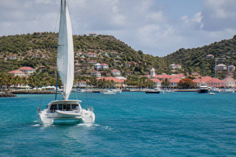 A sailing catamaran on open turquoise water approaching the coast of St Barts