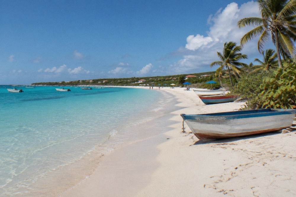 A long pale sand beach with calm shallow water and a few beach umbrellas along the shore