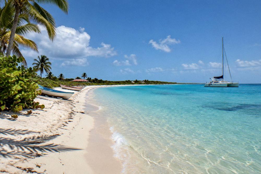 A catamaran at anchor in a quiet bay with clear shallow water over sand