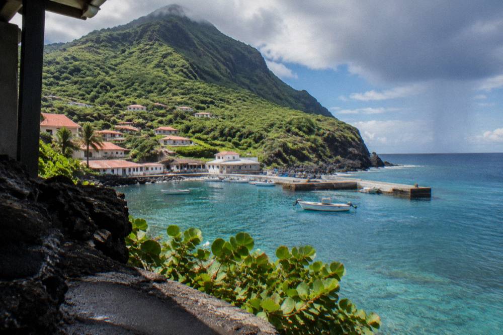 Small Caribbean island coastline with turquoise shallows and a passing rain cloud