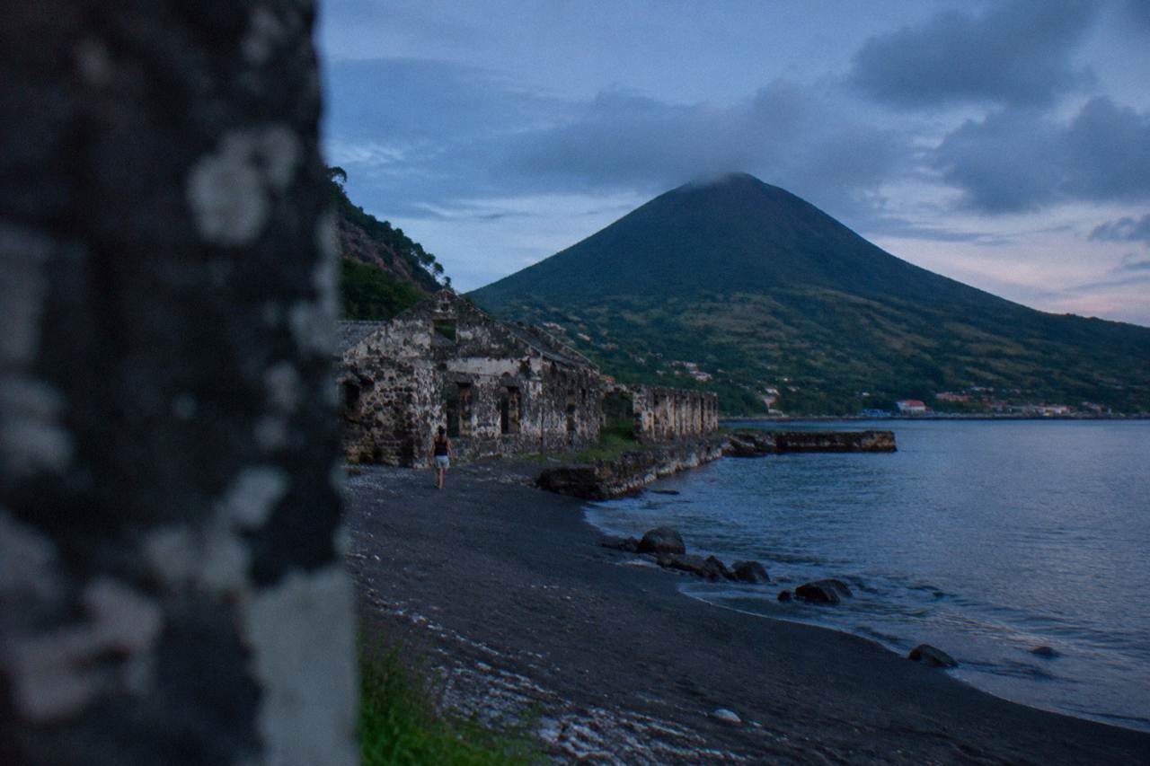 A small Caribbean island with a volcanic cone rising above a quiet coastline of green hills and blue water