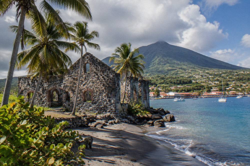 A stone ruin of an old Caribbean warehouse standing among palm trees near a harbour