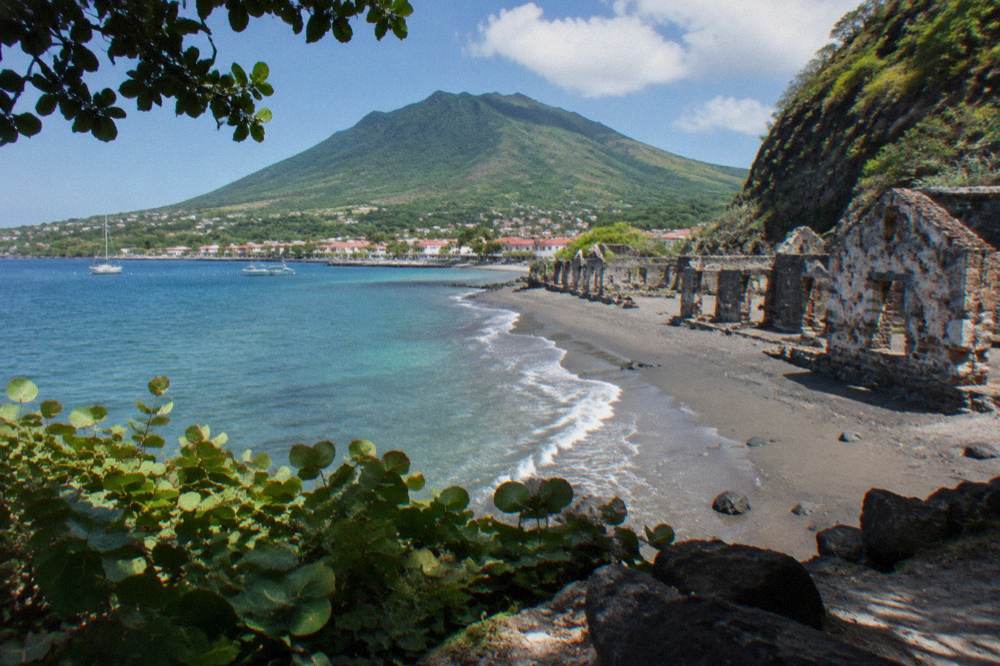 A forested volcanic crater rim seen from a trail above a small Caribbean town