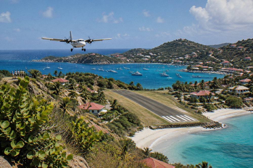 A small turboprop aircraft on a short runway beside a Caribbean beach
