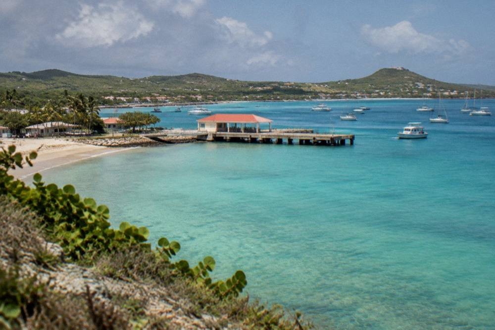 Sunlight on calm turquoise shallows over pale sand seen from a low clifftop