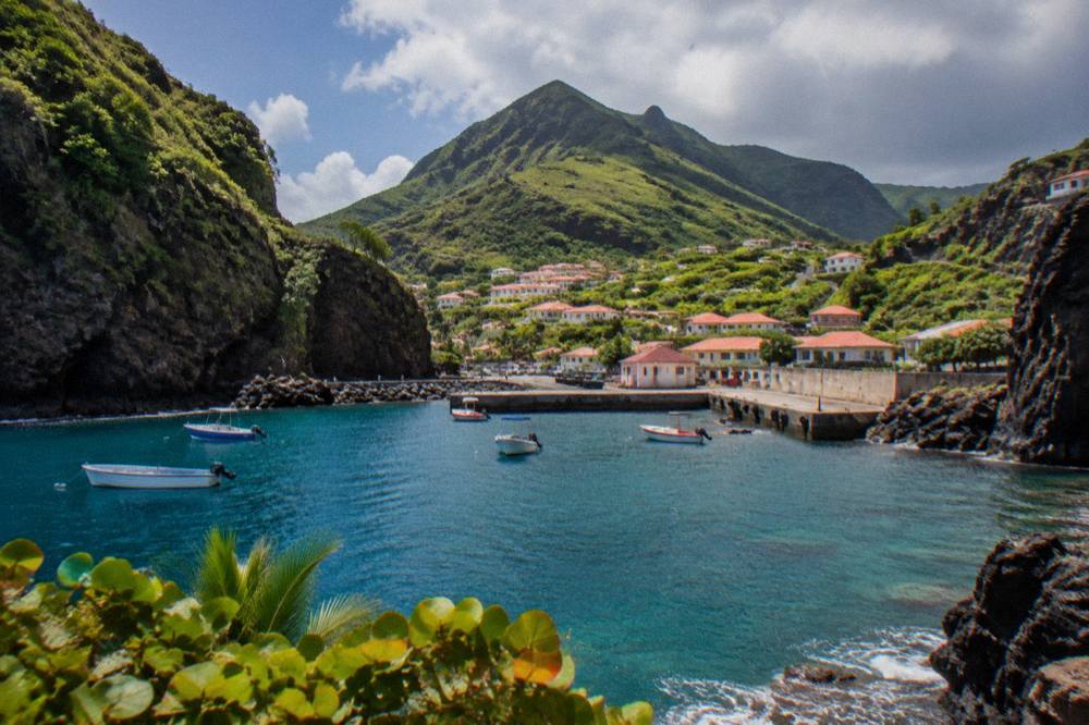 A Caribbean hillside town with red roofs and green peaks under scattered clouds