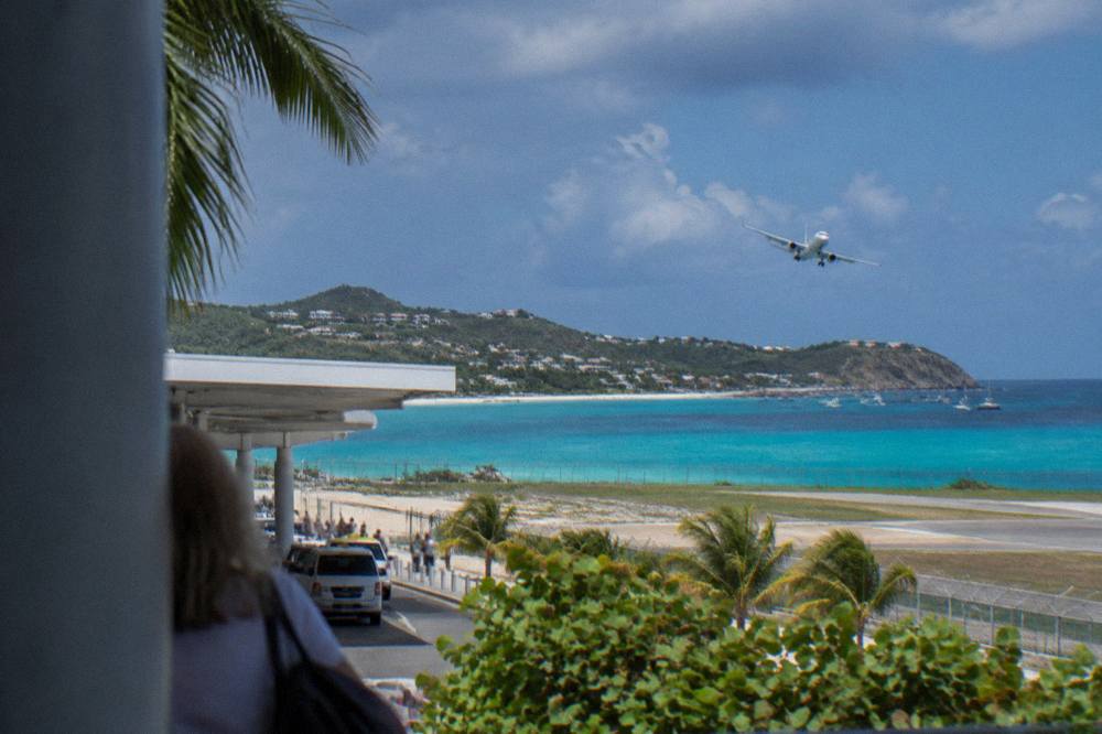 A small passenger plane banking over turquoise Caribbean water toward an island shoreline