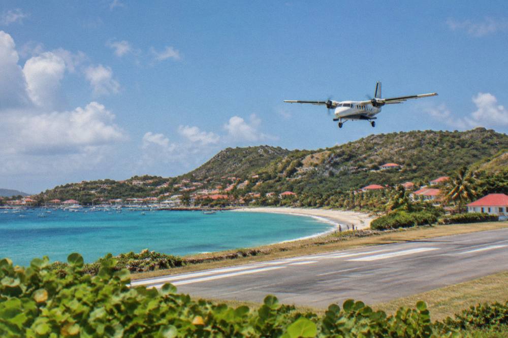 Turboprop airplane on a short runway beside a Caribbean beach with hills behind