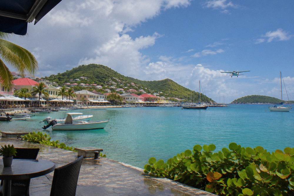 Small airplane flying low over turquoise water toward a green Caribbean island