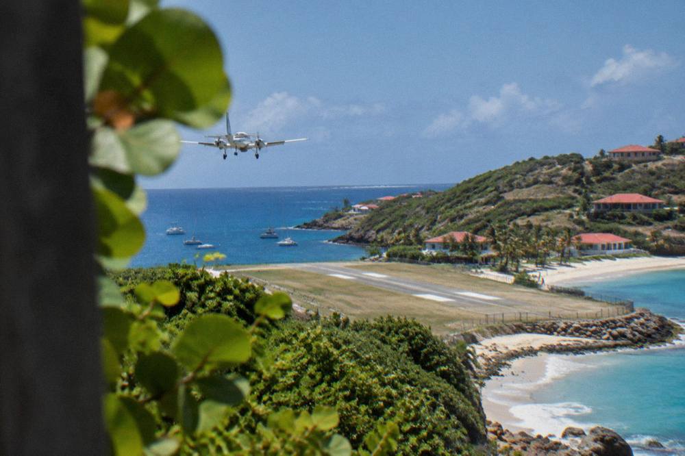 A small turboprop aircraft on a short runway between a green hillside and a beach