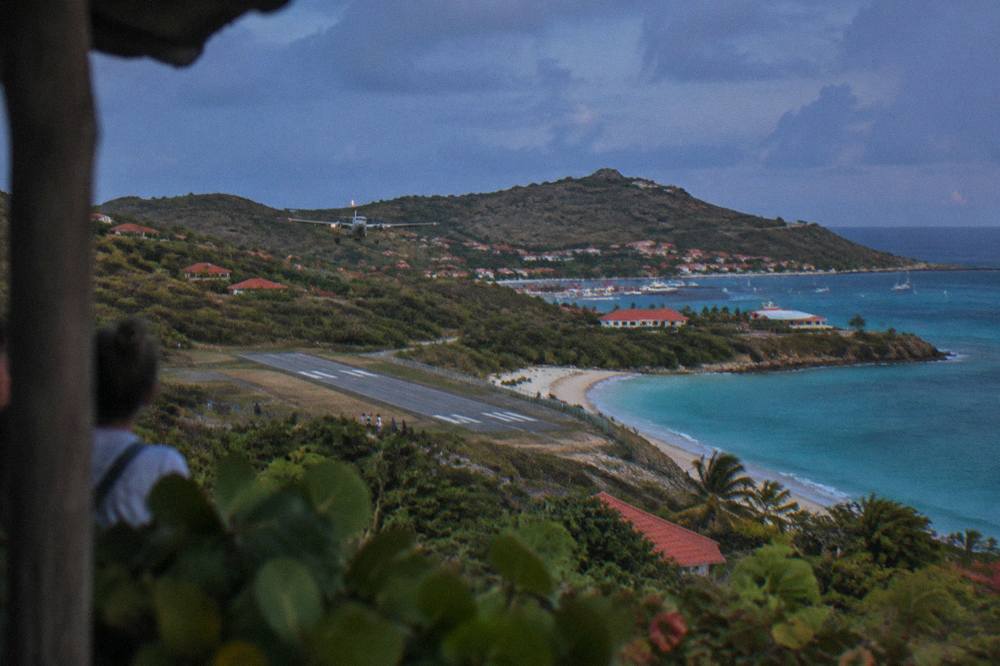 A small plane on a short runway beside a beach and turquoise bay seen from a hillside