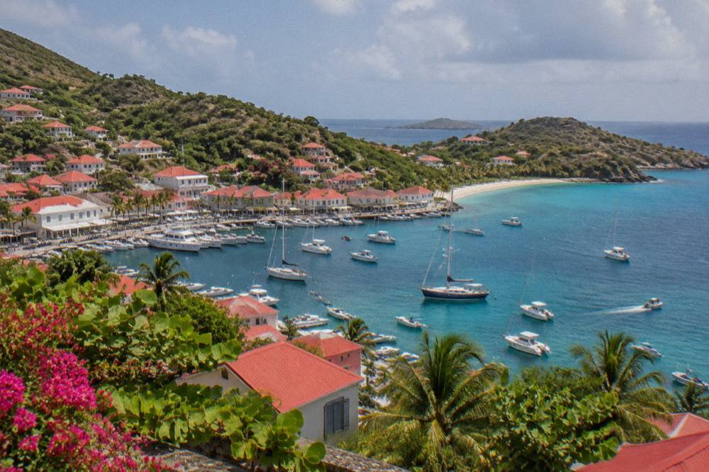 A quiet curved bay with turquoise shallows, a sandy shore and low green hills