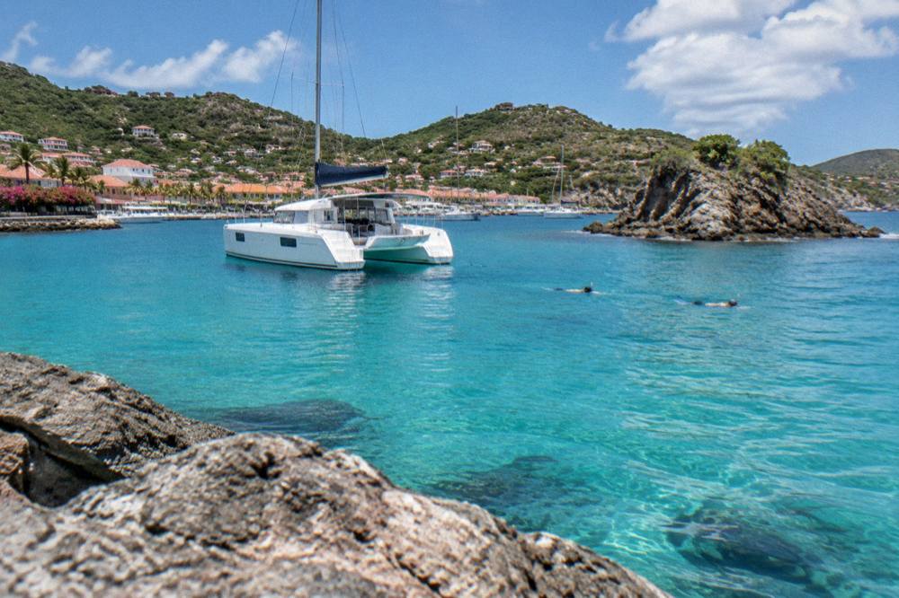 A catamaran anchored in clear water near a rocky islet with snorkelers nearby