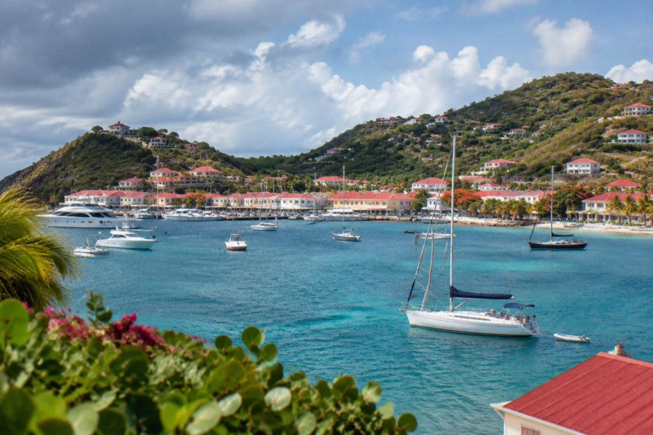 Sailboats anchored in turquoise water below green hills on a Caribbean island coastline