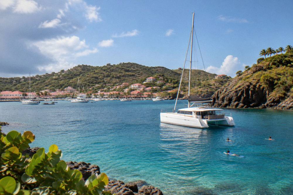 A catamaran moored in a quiet bay with snorkelers near rocky headland