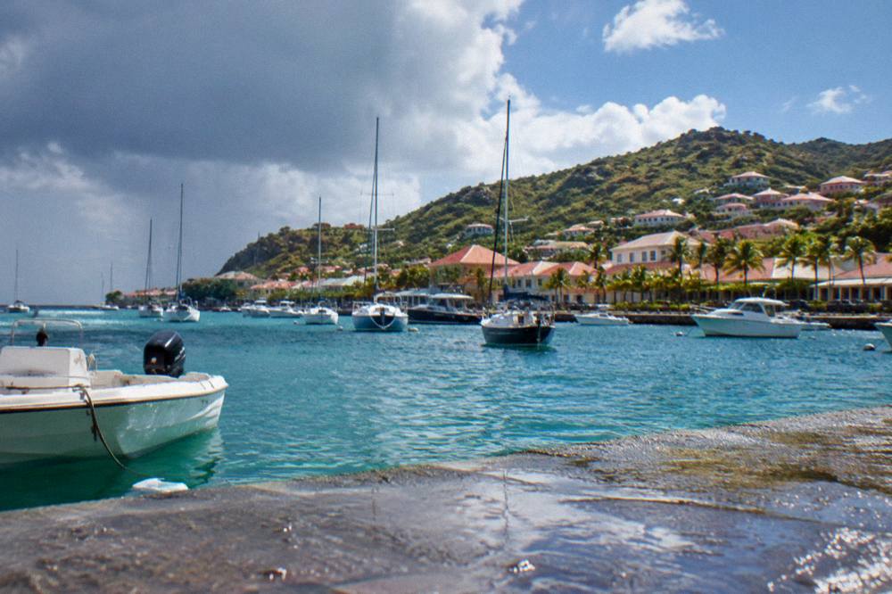 Red-roofed houses rising up a hillside above a small harbour with masts
