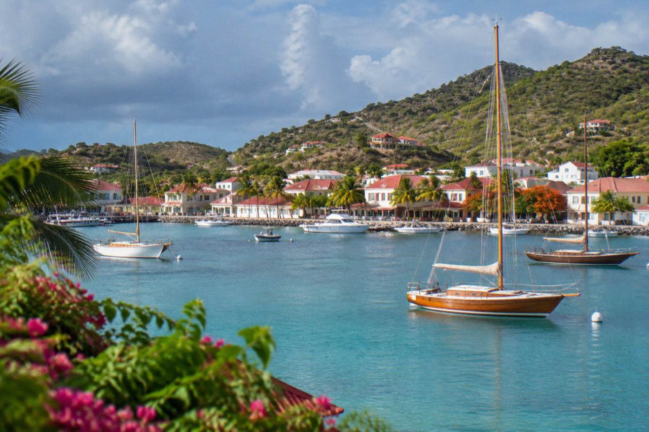 Wooden sailboats anchored in turquoise water below the hills of a small Caribbean harbour town