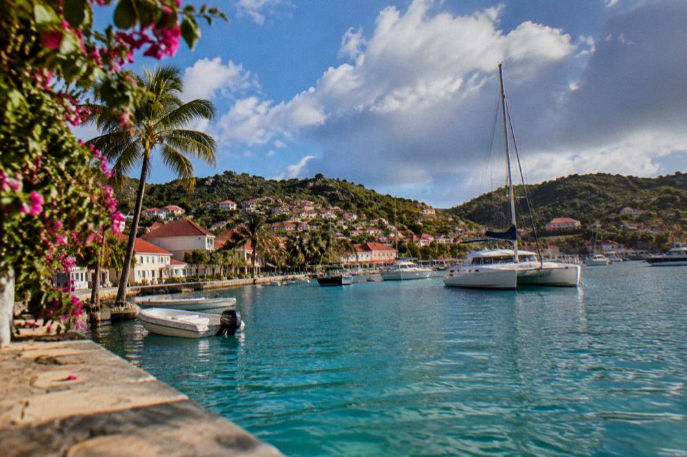 A catamaran and small boats moored in a clear bay ringed by green headlands