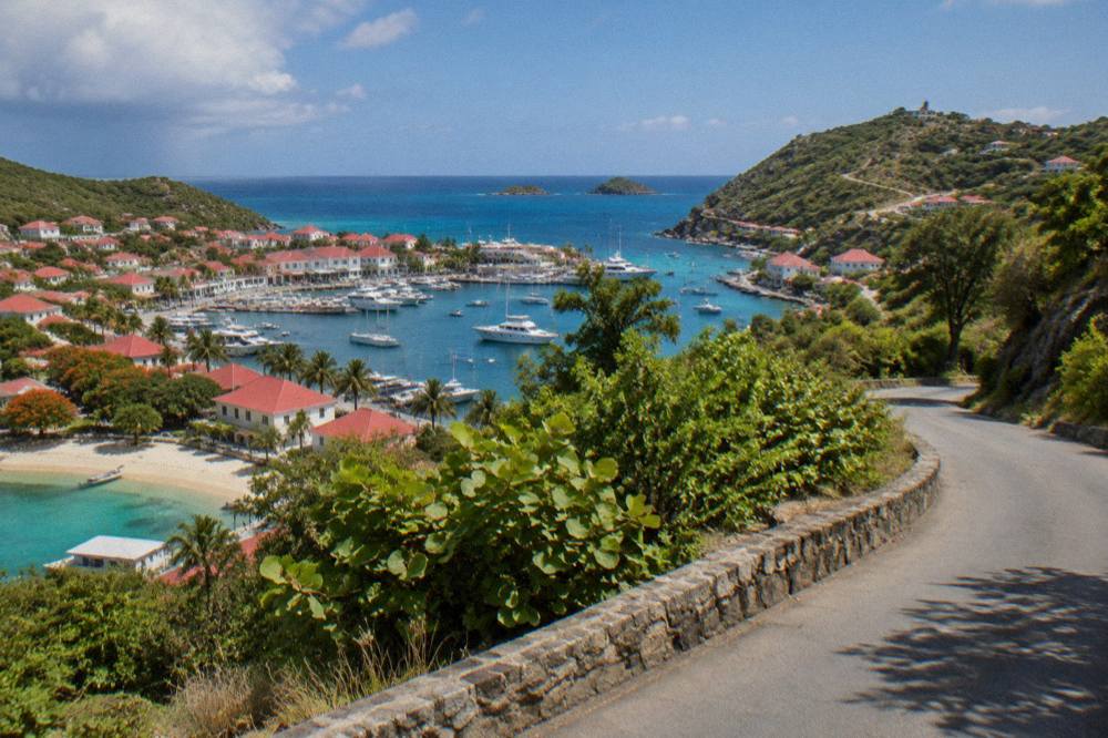 An empty narrow road curving between green hills above the Caribbean sea