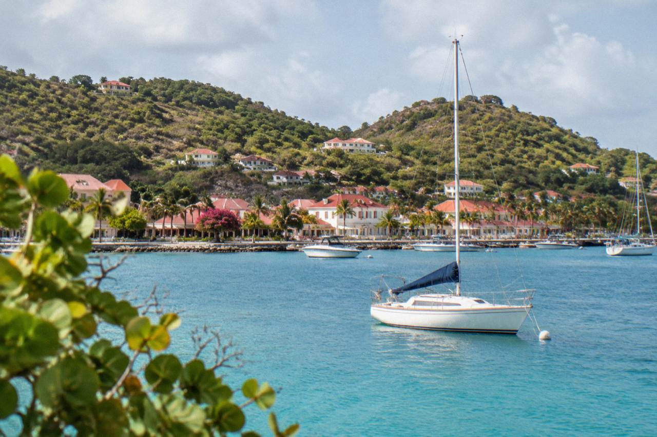 A small sailboat anchored in turquoise water off a green hillside on St Barts