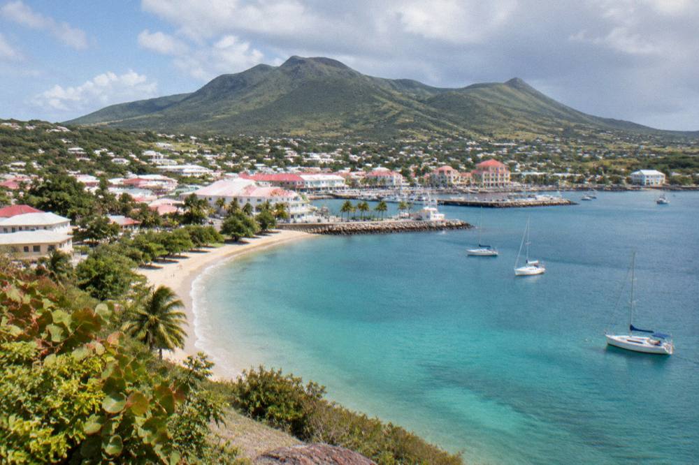 A green hillsides bay with a sandy beach and a few anchored sailboats