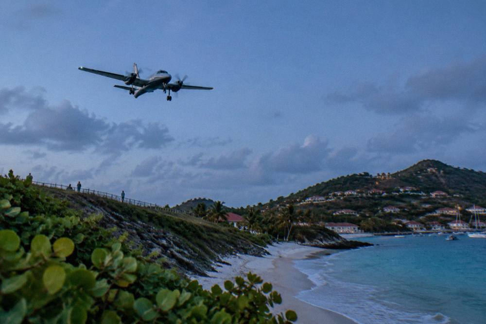 A small turboprop aircraft on a short runway beside a Caribbean beach