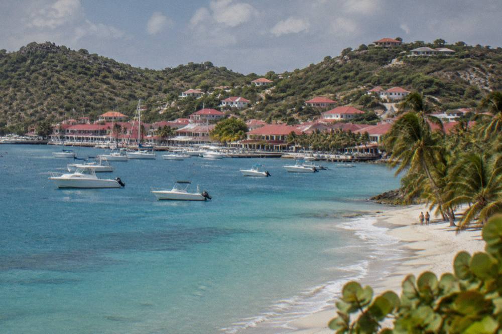 A quiet Caribbean beach with white sand and a few palm trees in late afternoon light