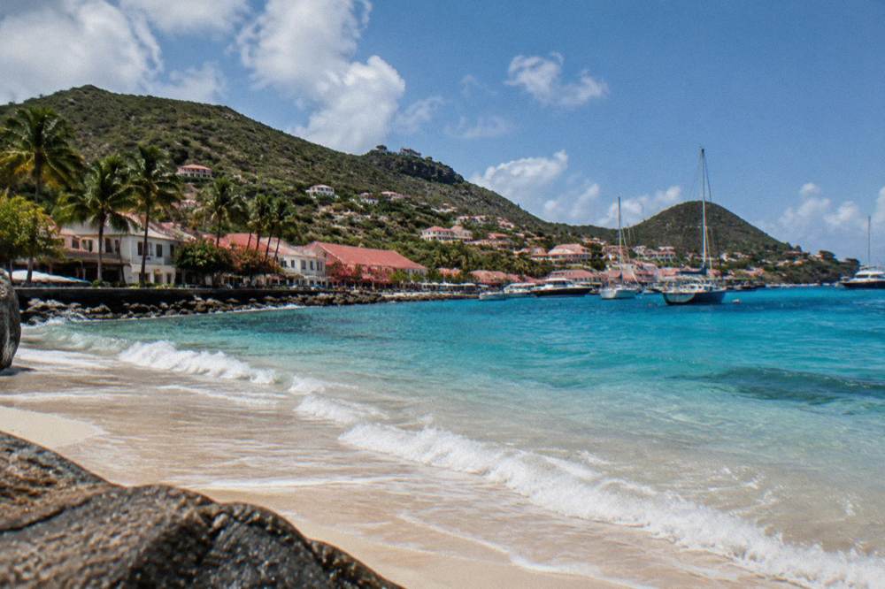 An east coast shoreline on St Barts with waves reaching a strip of sand below green hills