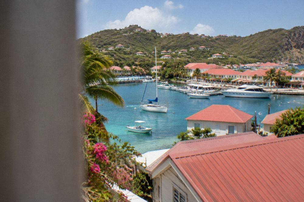 A sailboat anchored off a green headland on St Barts with clear water over the shallows