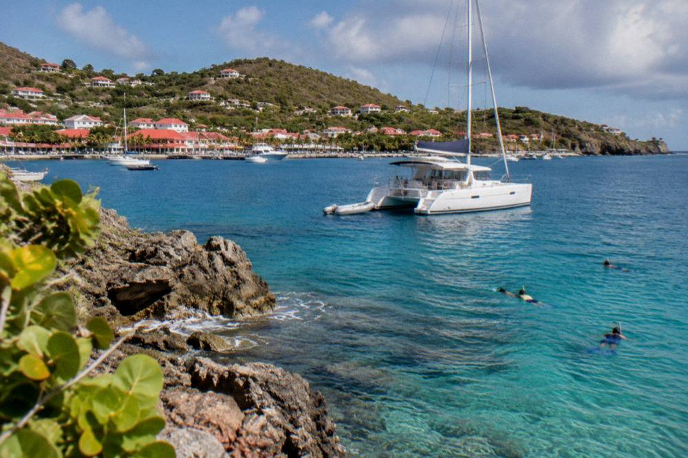 A sailing catamaran anchored in a rocky bay in St Barts with snorkelers in the water