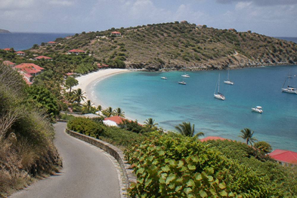 A narrow winding road descending toward a bay on a green hillside in St Barts