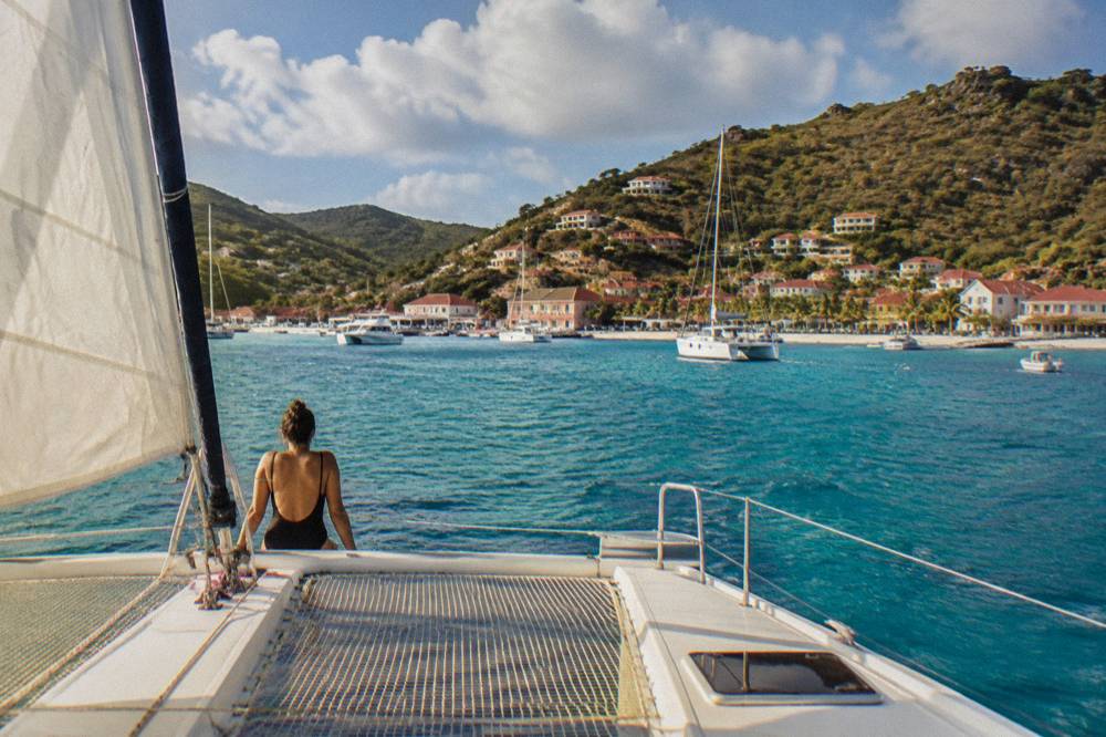 A catamaran under sail approaching a green hillside anchorage near St Barts