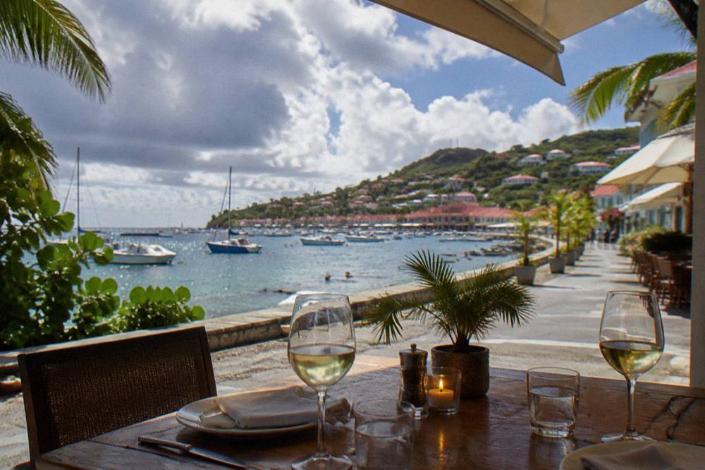 An evening table set with glasses overlooking a lit harbor below
