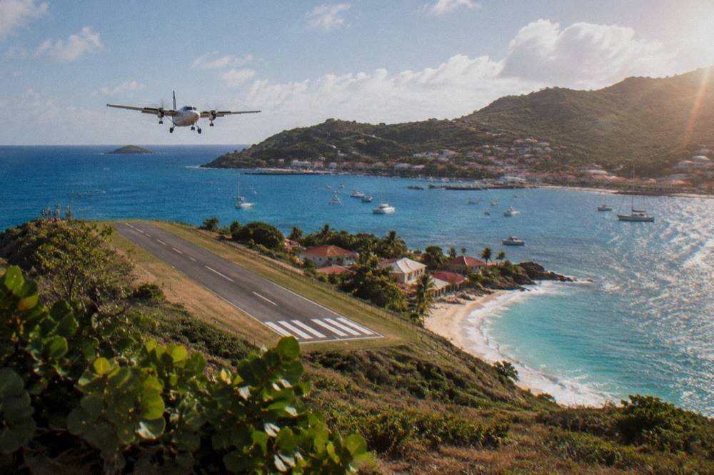 A small turboprop aircraft on a short runway beside a Caribbean beach