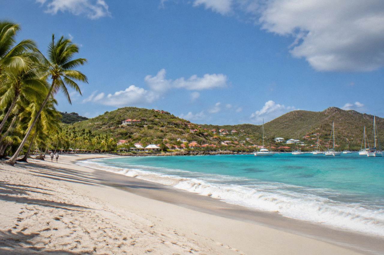 White hotel buildings and palm trees above a crescent beach with calm turquoise water