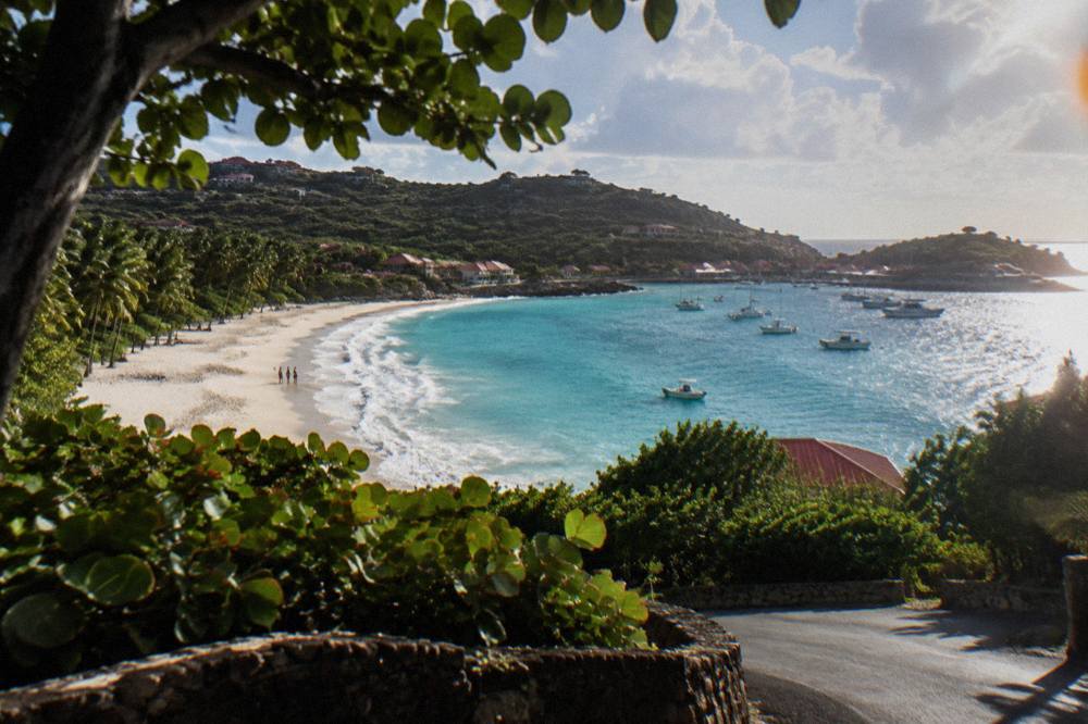 A narrow hillside road curving down toward a turquoise bay with red-roofed houses
